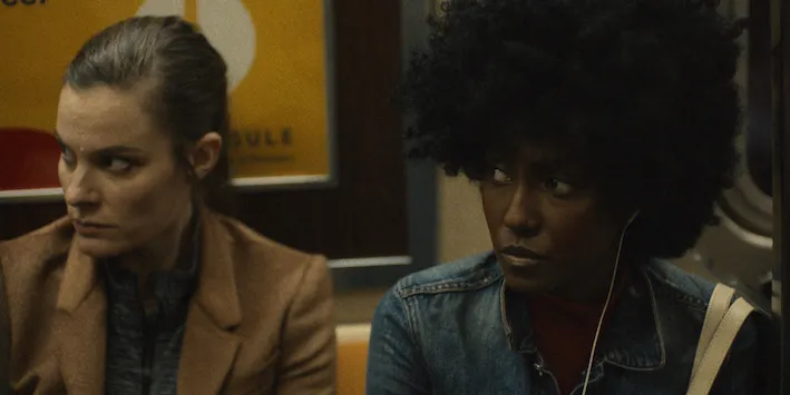 A white woman sitting next to a Black woman on the subway, both looking suspiciously to the left.