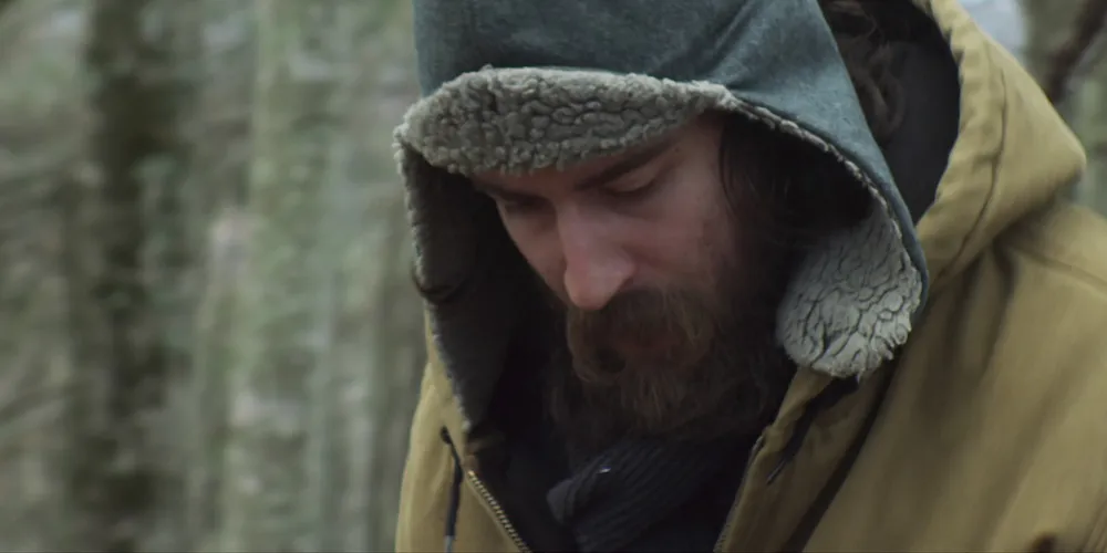 A man with a beard in the woods.