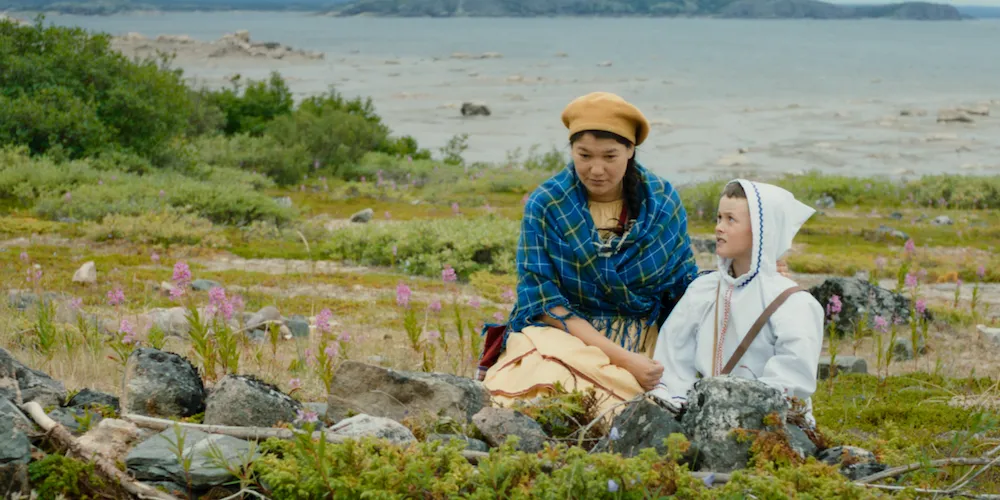A woman sitting with someone smaller by the water.