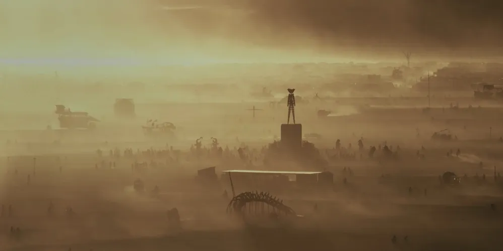 A desert landscape at Burning Man, with the wooden Man effigy towering over a crowd at sunset.