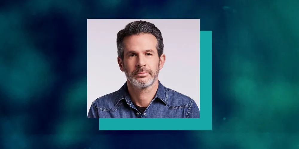Headshot of Simon Kinberg in a denim shirt with a blue and turquoise border. 