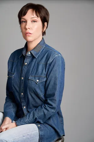 White woman with short hair and a denim long sleeve shirt sitting with a serious pose