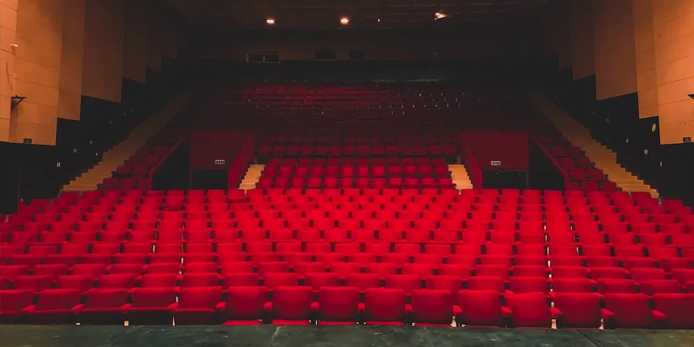 View of where the audience sits in a theater -- very velvet red chairs. 