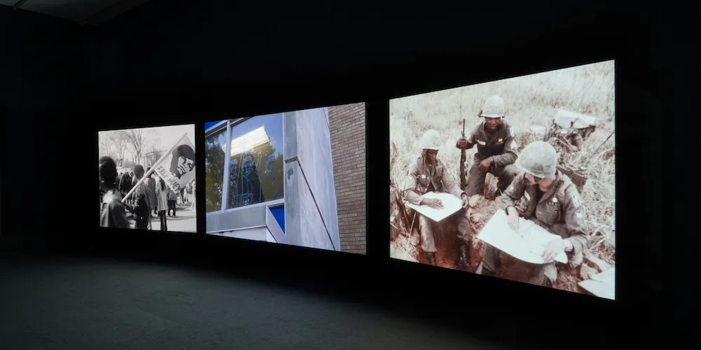 Three large screens displaying images against a black wall. 