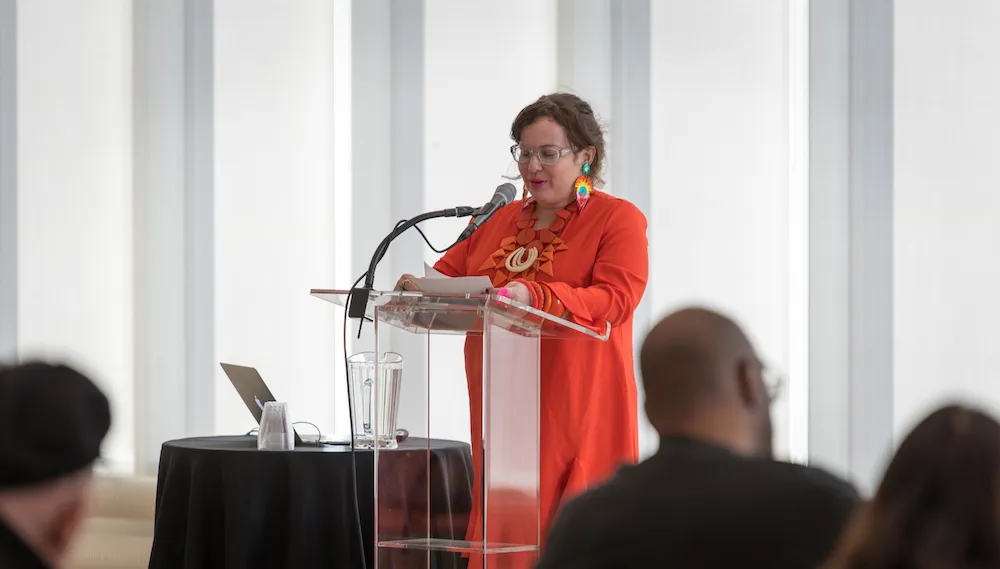 Photo of a woman in orange at a podium. 