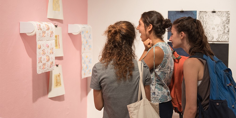 women looking at paper towel art on pink wall