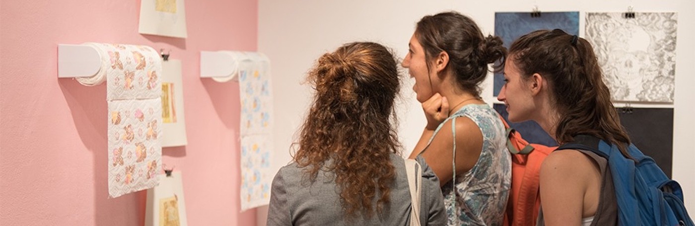 Three students view painted paper towels against a pink wall