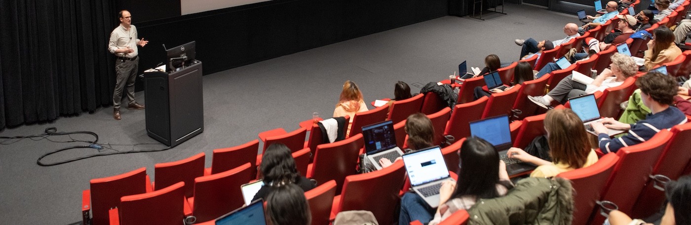 Professor Rob King teaches at a podium in front of an auditorium of students