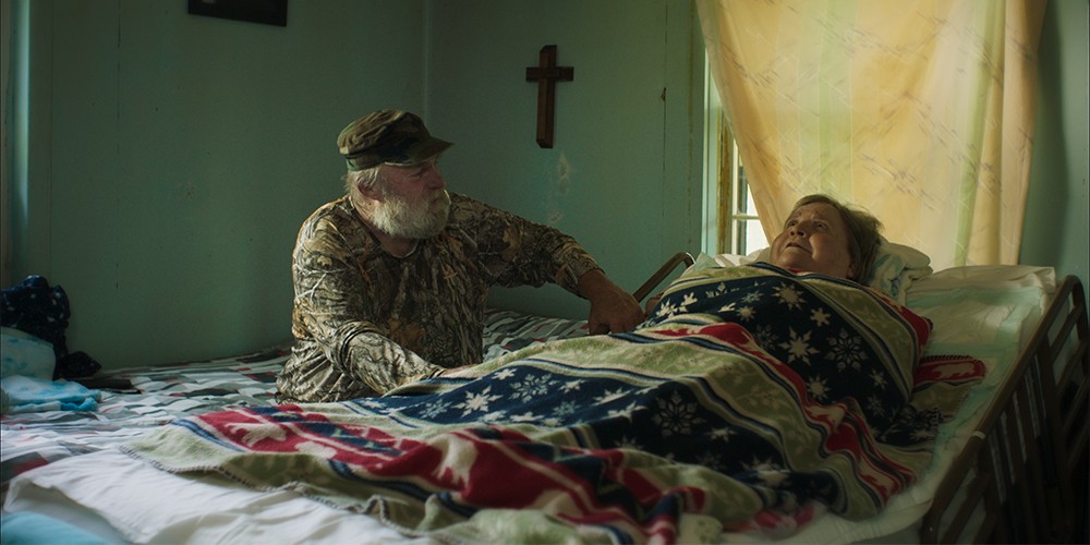 still from "If Dreams Were Lightning: Rural Healthcare Crisis"of woman lying in hospital bed with man sitting beside her