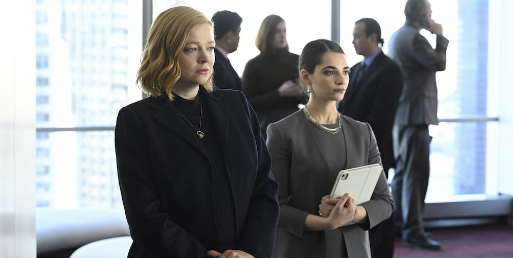 Two women in business suits looking ahead with a group of people behind them. 