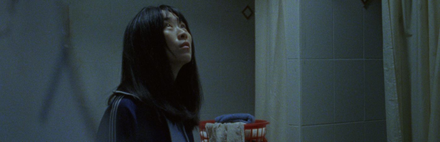 Woman in dimly lit bathroom looks up. 