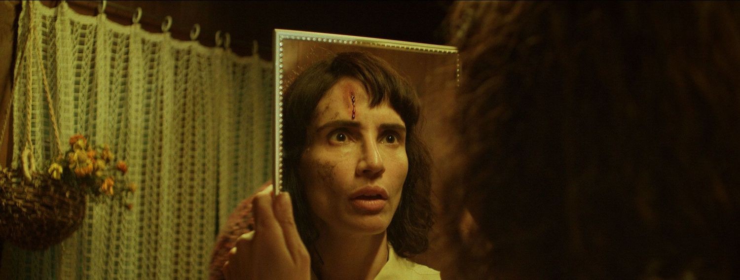 Still from The Cow Who Sang a Song Into the Future, a woman looks at her face in a mirror, looking frightened. 