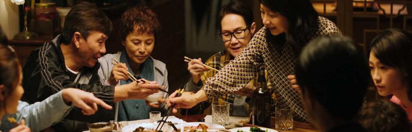 A group of people eating with chopsticks around a table full of food. 