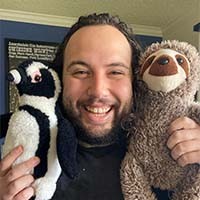 man with brown hair and beard holding a sloth and penguin stuffed animals.