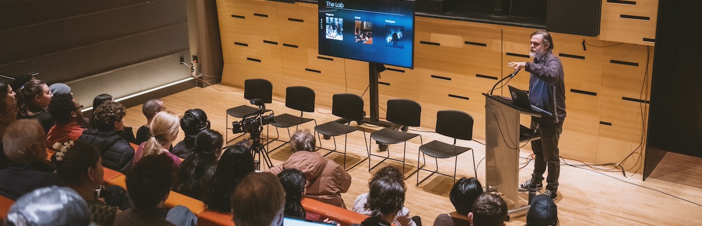 A professor teaches from a podium to an auditorium of students