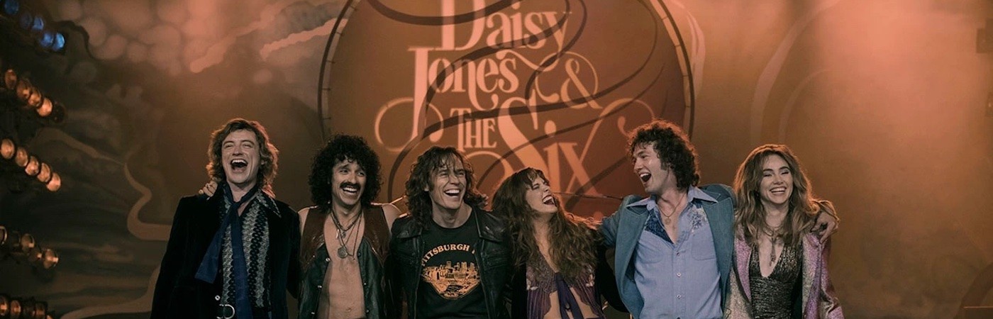 Still from Daisy Jones and the Six - band members lined up on a stage, laughing. 