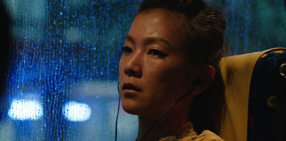 Woman with headphones in front of dark, rainy window