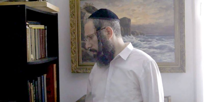 Still from 'The Binding of Itzik' Man looking at bookshelf