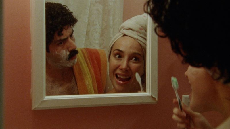 man shaving, woman with toothbrush viewed in mirror reflection
