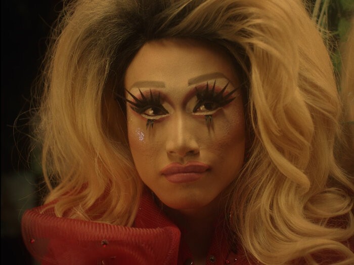 Still from 'Coronation' character with elaborate makeup and hair