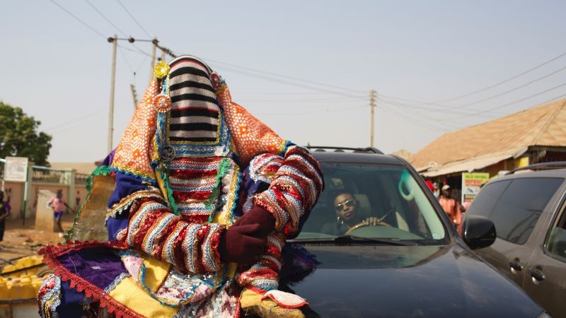 costumed figure seated on hood of car