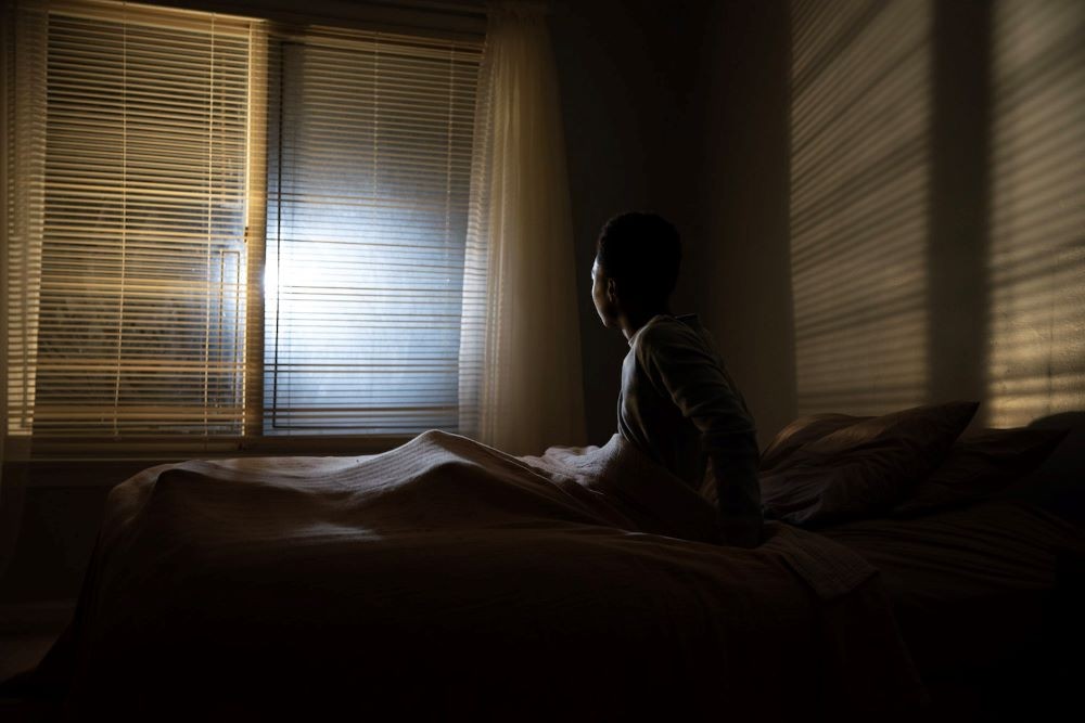 Still from 'Home' Silhouette sitting up in bed looking at bright light through blinds