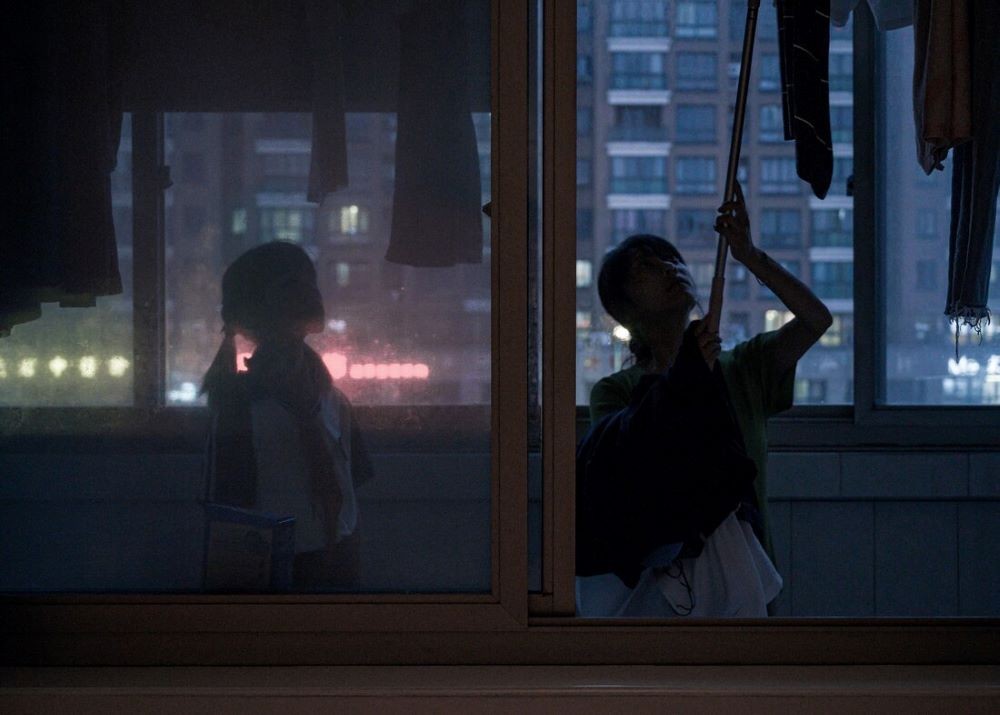 Two people standing in front of an opening window at night
