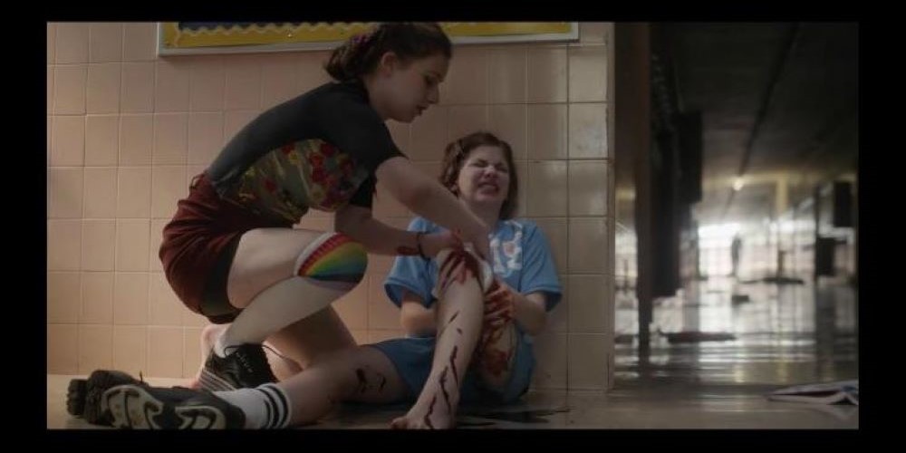 Two girls in school hallway, one with bloodied leg