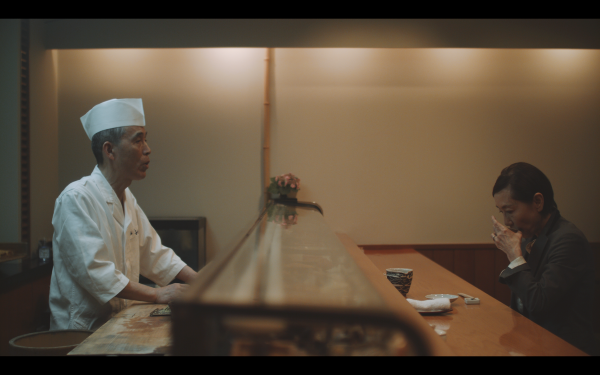 Person seated across a bar from a chef