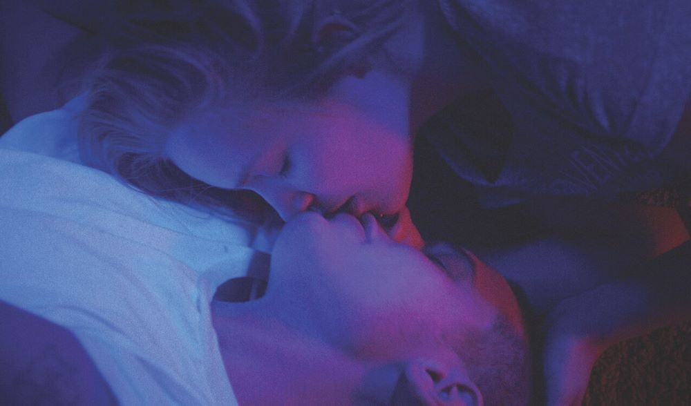 Two individuals kissing under purple lighting