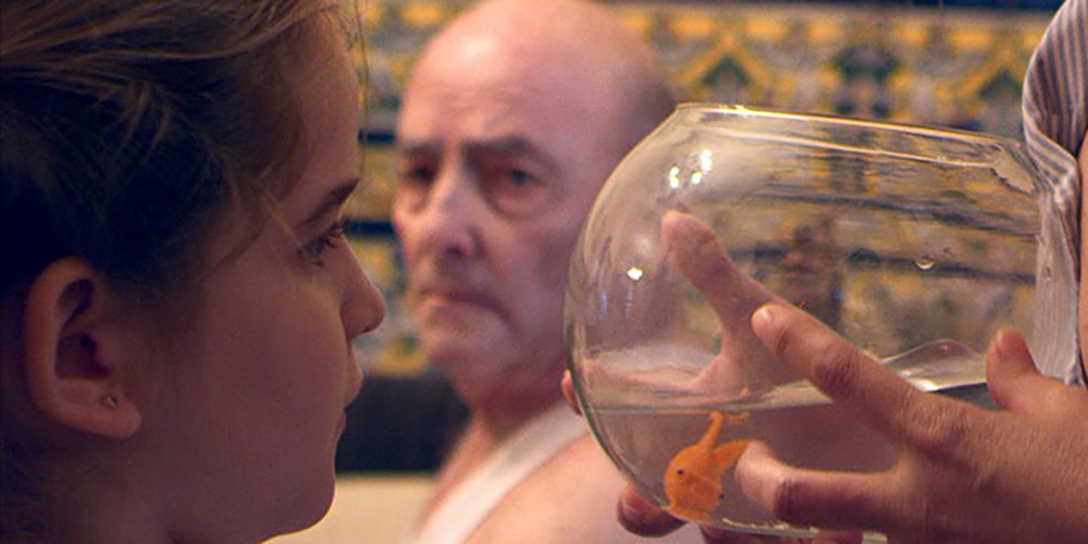 Still from 'Something to Believe In (Algo en lo que creer)'. A little girl looks at a fish in a fish bowl.
