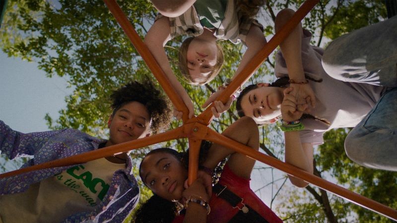 four children on jungle-gym looking down at camera