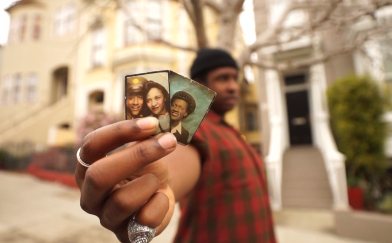 A black man shows small photographs to the camera.