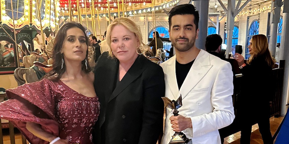 Two women and a man stand in front of a carousel. 