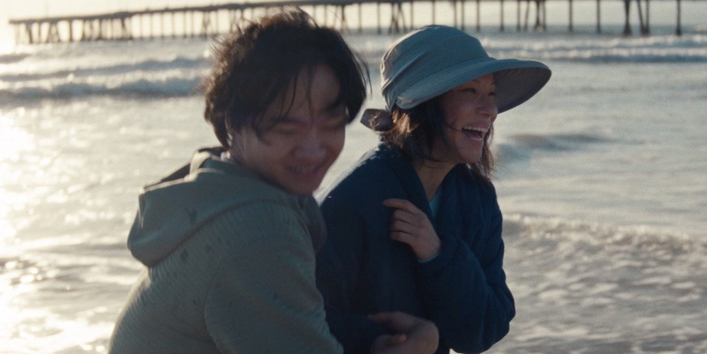 a young man and woman walk arm in arm along the beach