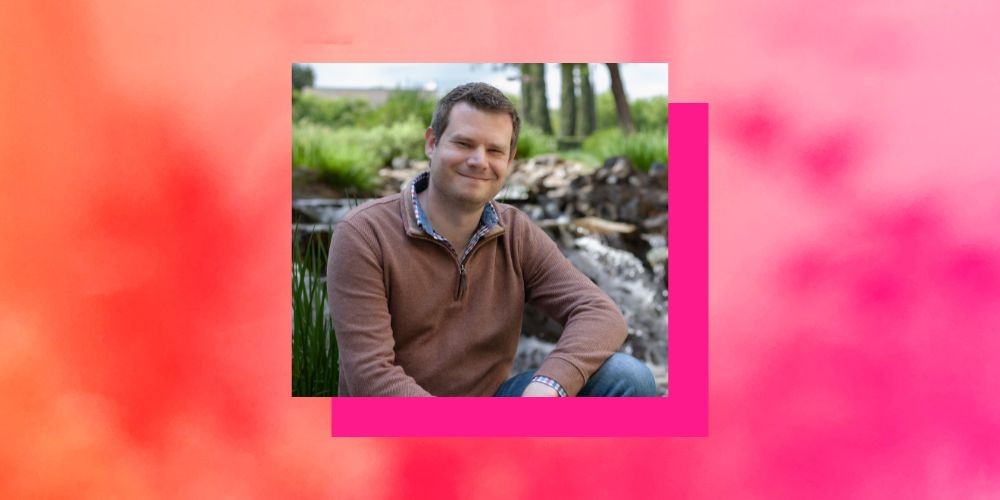 Headshot of a man in a brown sweater in front of waterfall, with a orange and pink boarder. 
