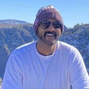Man with a beanie and glasses smiling on a mountain
