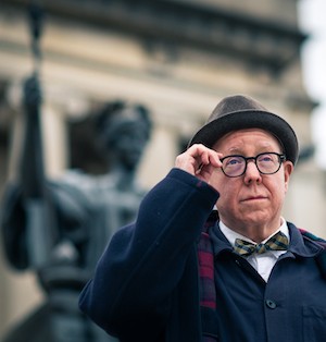 James Schamus stands in front of Columbia's Alma Mater statue, adjusting his glasses. 