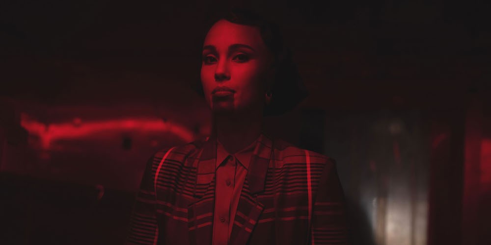 Woman stands under dark red lighting. 