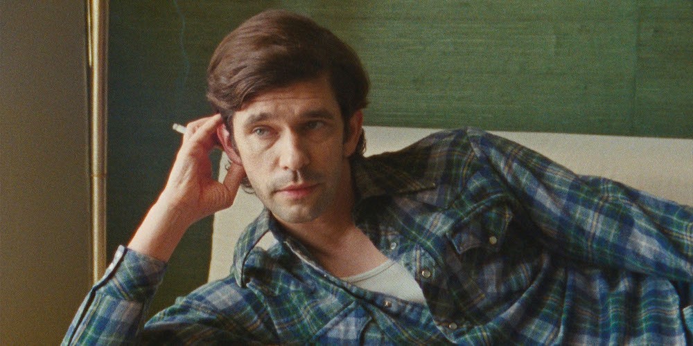 Man holding a cigarette leans on a couch. 