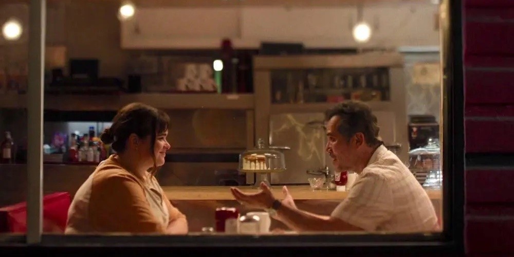 A man and young women sit talking in a diner. 