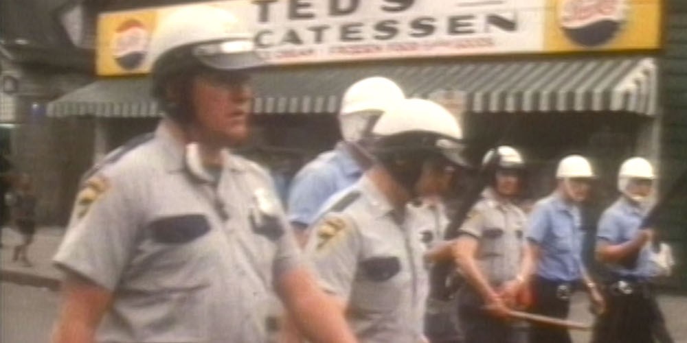 Police officers in older uniforms march down a street