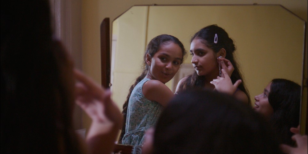 Three girls try on earrings in a mirror. 