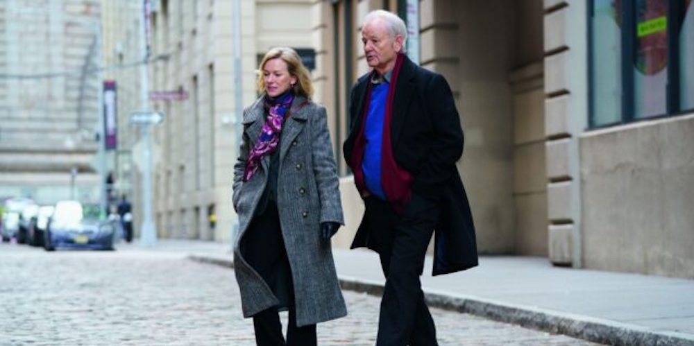 A man and woman in wool coats crossing a cobblestone street. 