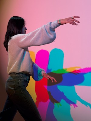 Woman posing in front of a projection of bold colors that become her shadow. 
