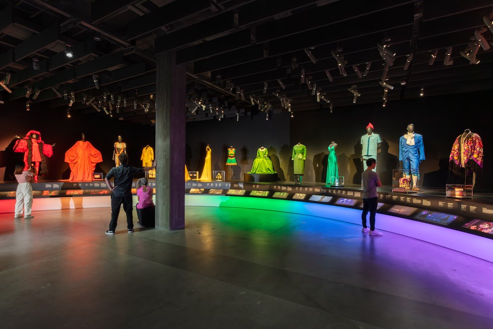 Viewers in large gallery space showcasing colorful clothes. 
