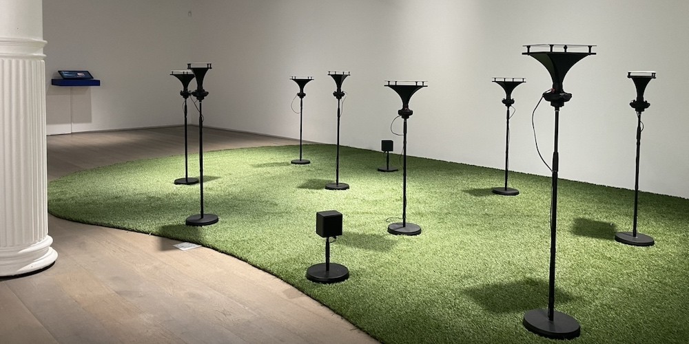 Gallery with astroturf and black speakers that mimic light poles in parks
