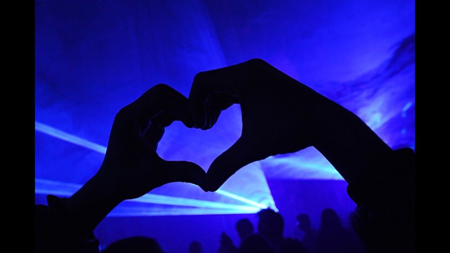 Hand sign in form of a heart over blue laser background.