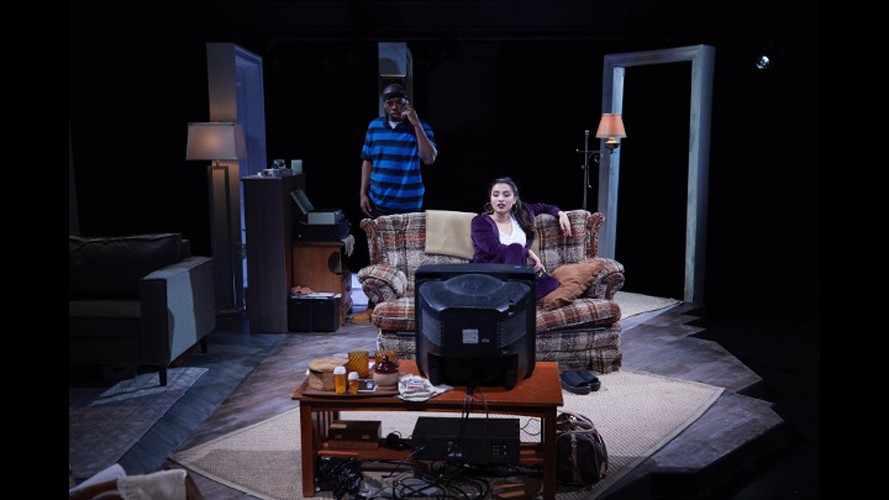 Photo of a play with a living room in scene and two actors.