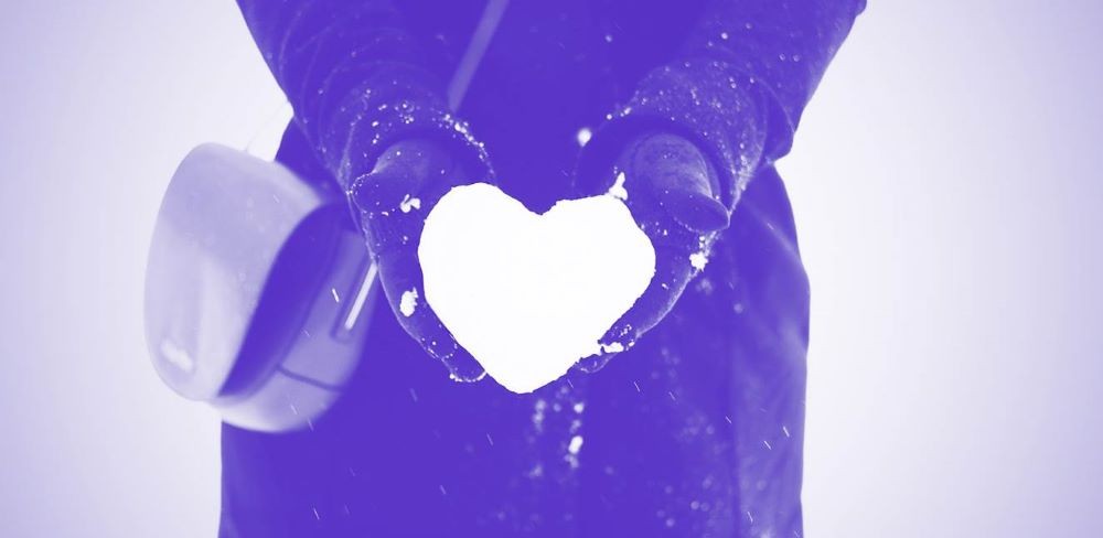 purple filtered photo of gloved hands extending heart made of snow